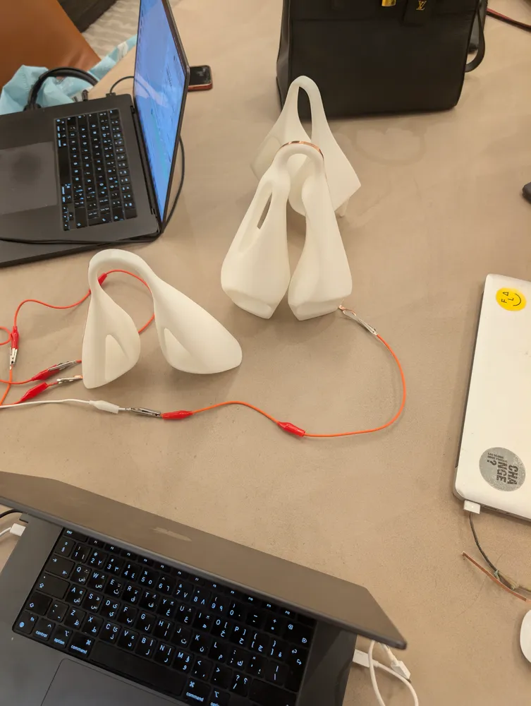 White 3D-printed prototypes wired with alligator clips beside two laptops
